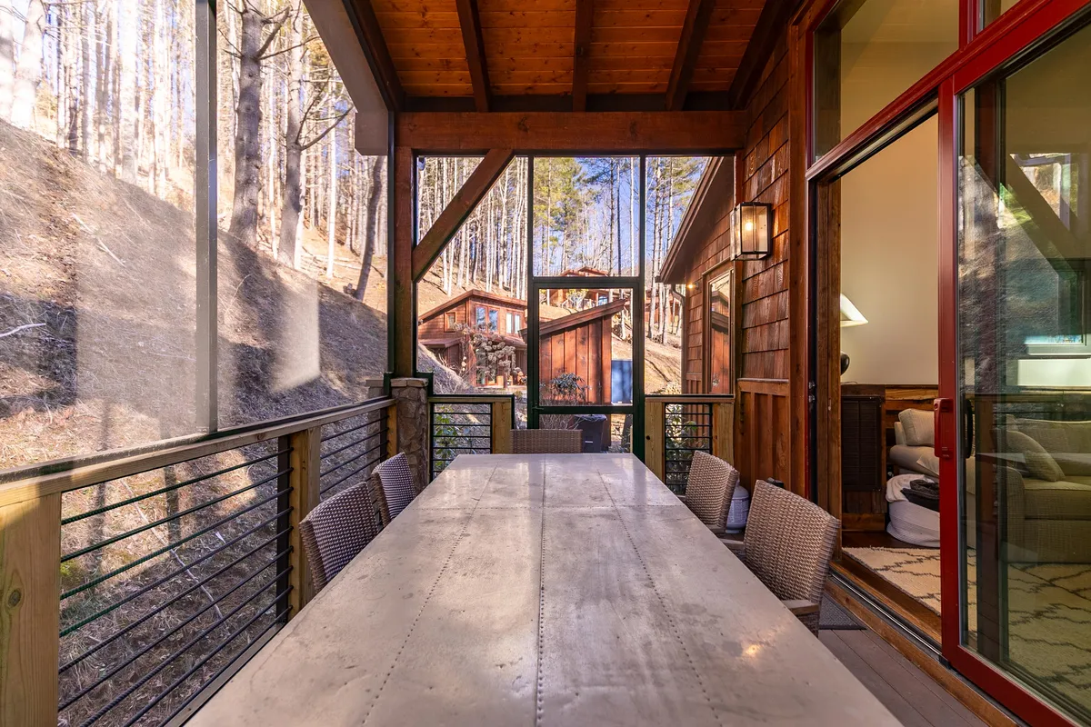 A long outdoor dining table sits under a wooden structure, with scenic views of lush greenery stretching beyond. This inviting space is perfect for pet-friendly outdoor dining and social gatherings.