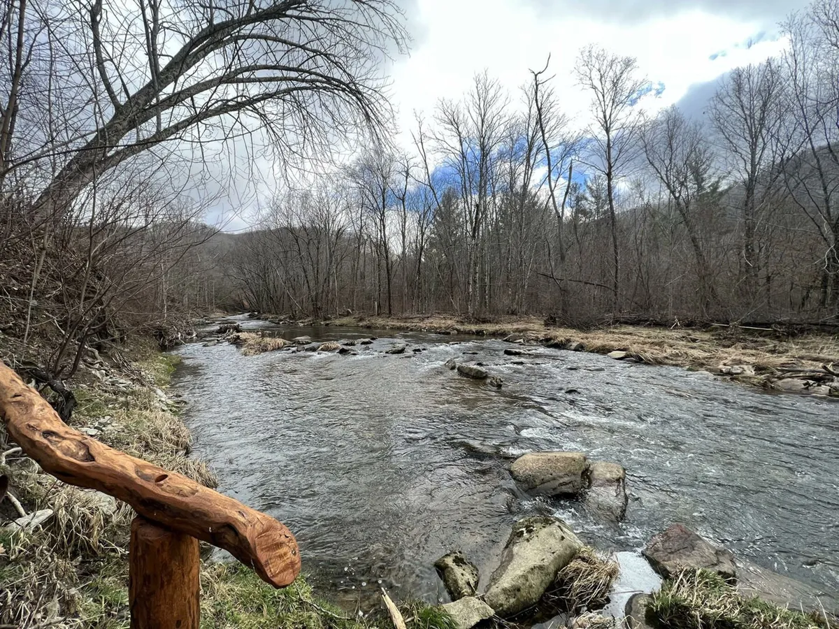 A serene riverside view with a flowing river, rock formations, and wooden railing inviting guests to enjoy nature. The setting is ideal for fishing, nature walks, and quiet reflection, with the untouched landscape emphasizing tranquility and exclusivity.