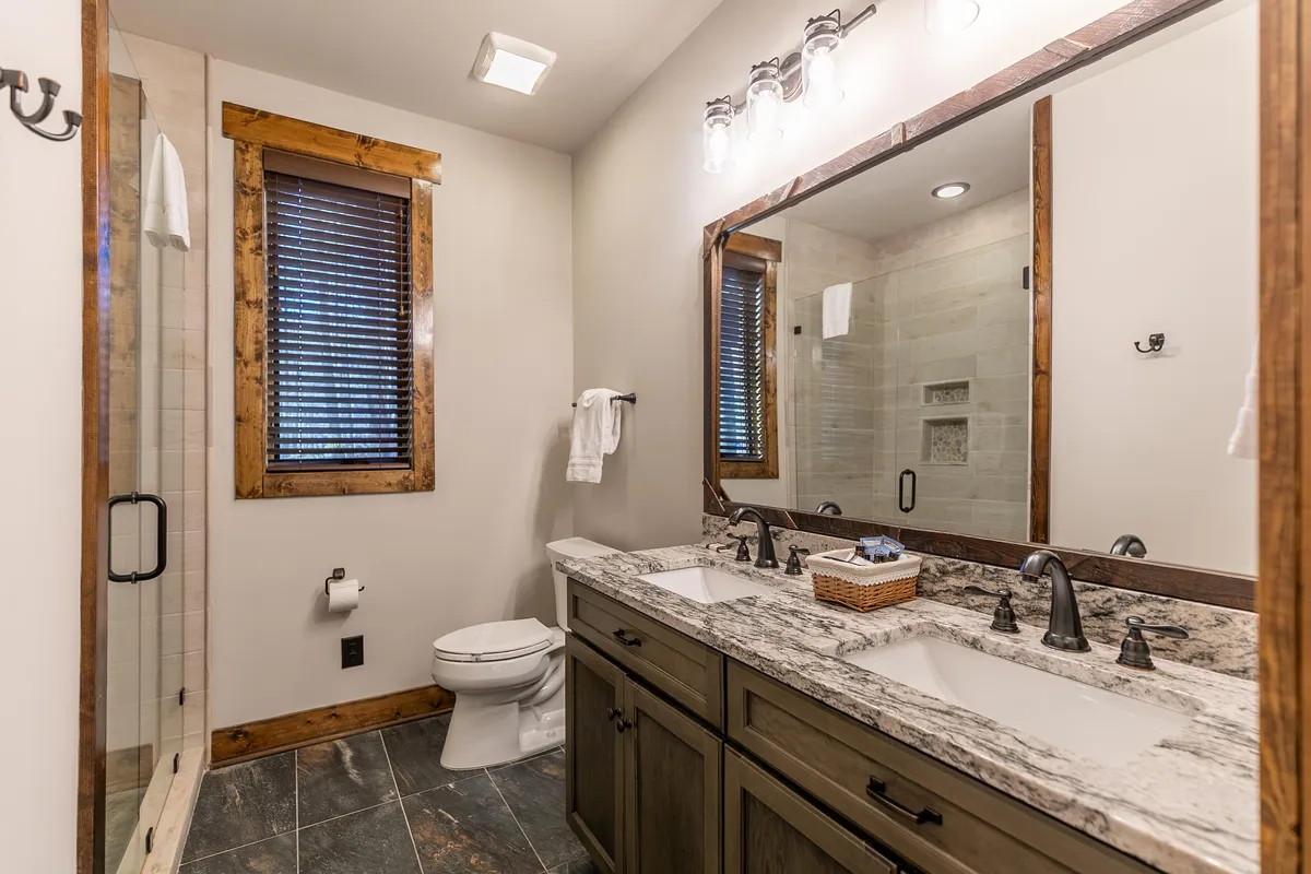 An elegant bathroom with a double granite vanity, a large mirror reflecting soft natural light, and a glass-enclosed, spa-like tiled shower. The modern finishes create a luxurious, self-care-focused environment in line with the ensuite's description.