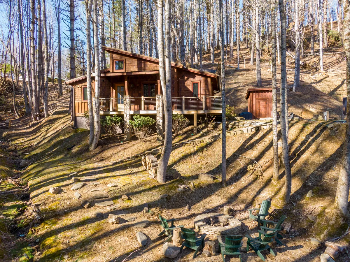 This image showcases a charming wooden cabin with inviting outdoor seating around a fire pit, set amidst tall trees. The scene suggests cozy evenings spent stargazing, sharing stories by the fire, or simply enjoying the crisp mountain air. The fire pit area directly alludes to fireside relaxation mentioned in the content.