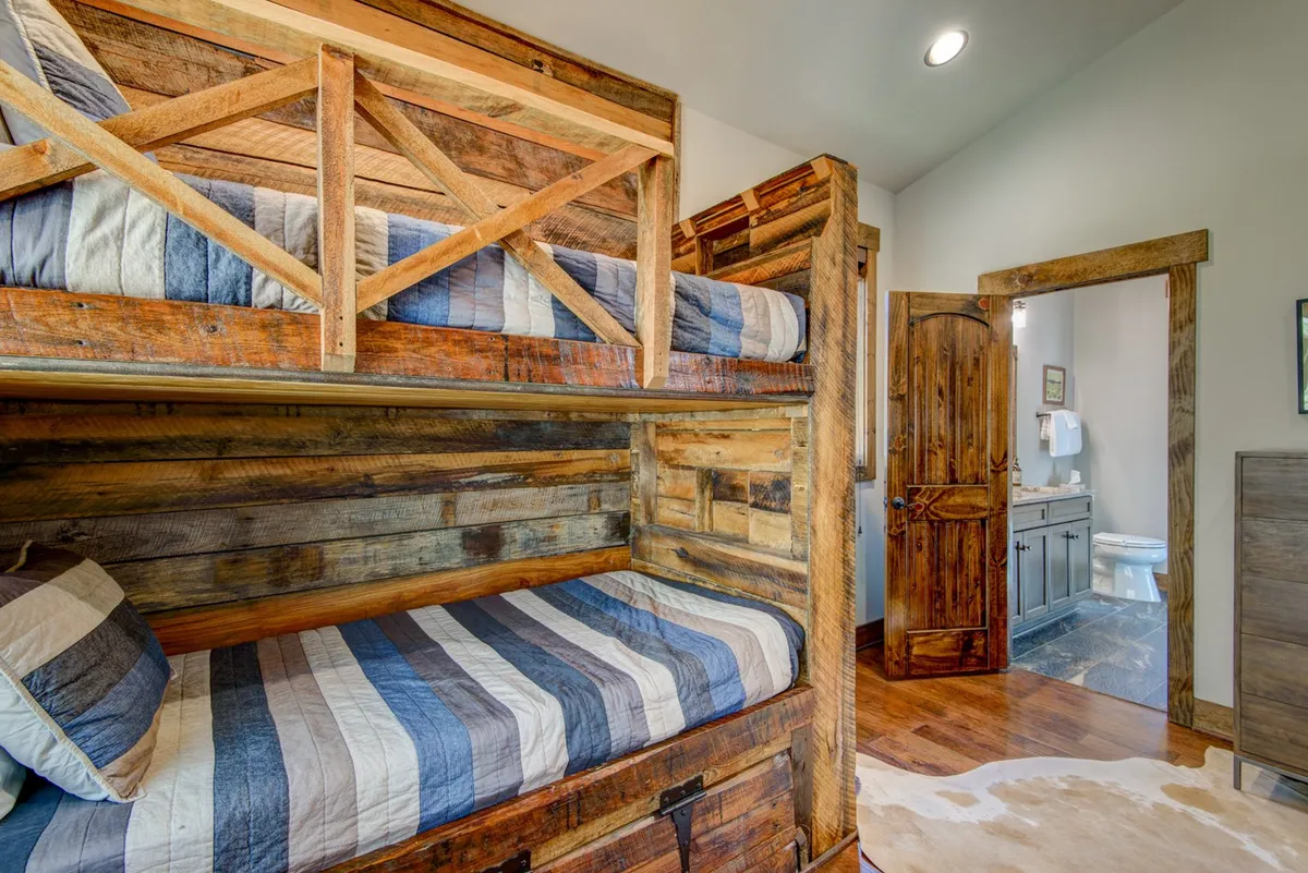 A warm, inviting bunk room with two sets of wooden bunk beds dressed in striped bedding, all surrounded by cozy wooden textures. The room exudes a playful, welcoming feel perfect for kids or friends to share late-night stories.