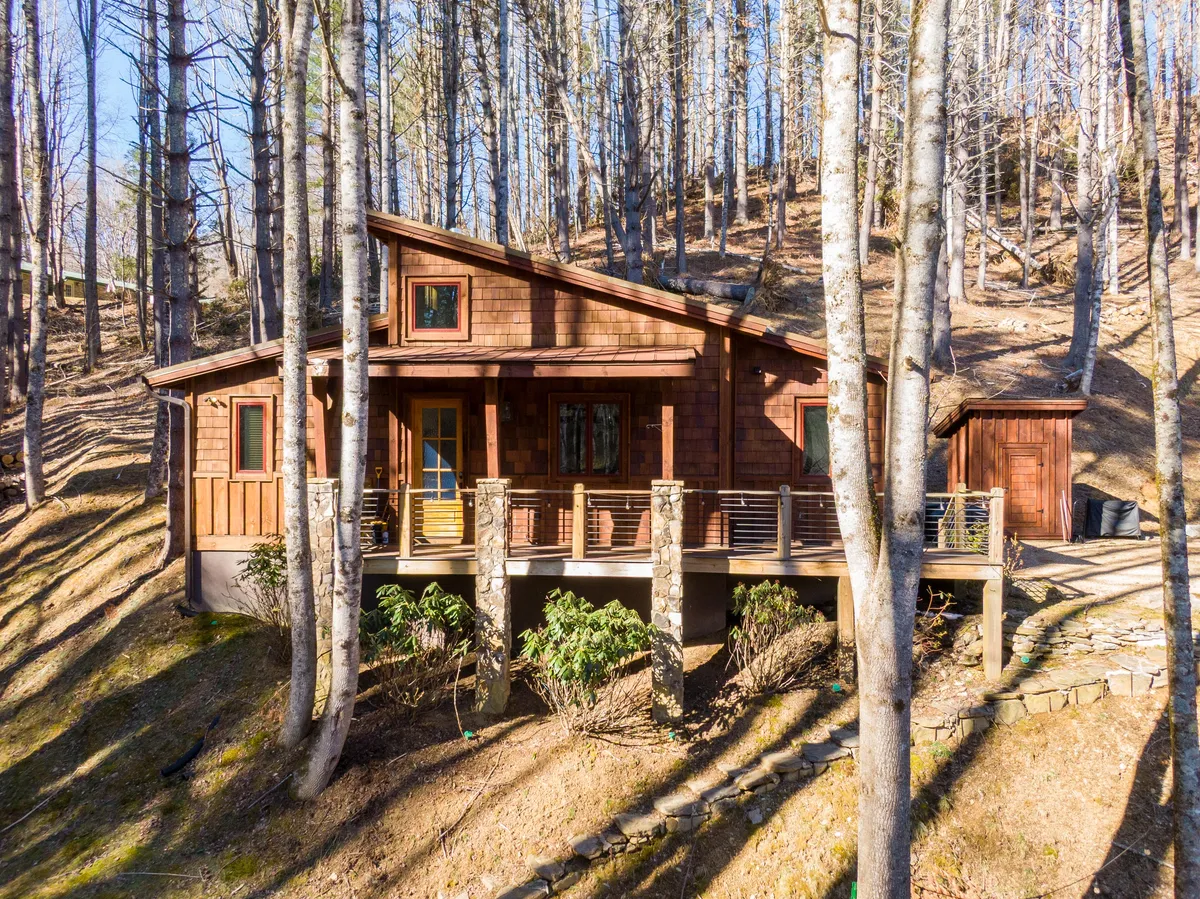 This image shows a cozy wooden cabin with a spacious deck and stone pillars, surrounded by tall trees. The setting is serene and natural, ideal for walks or resting with your dog after a fun day on the trails.