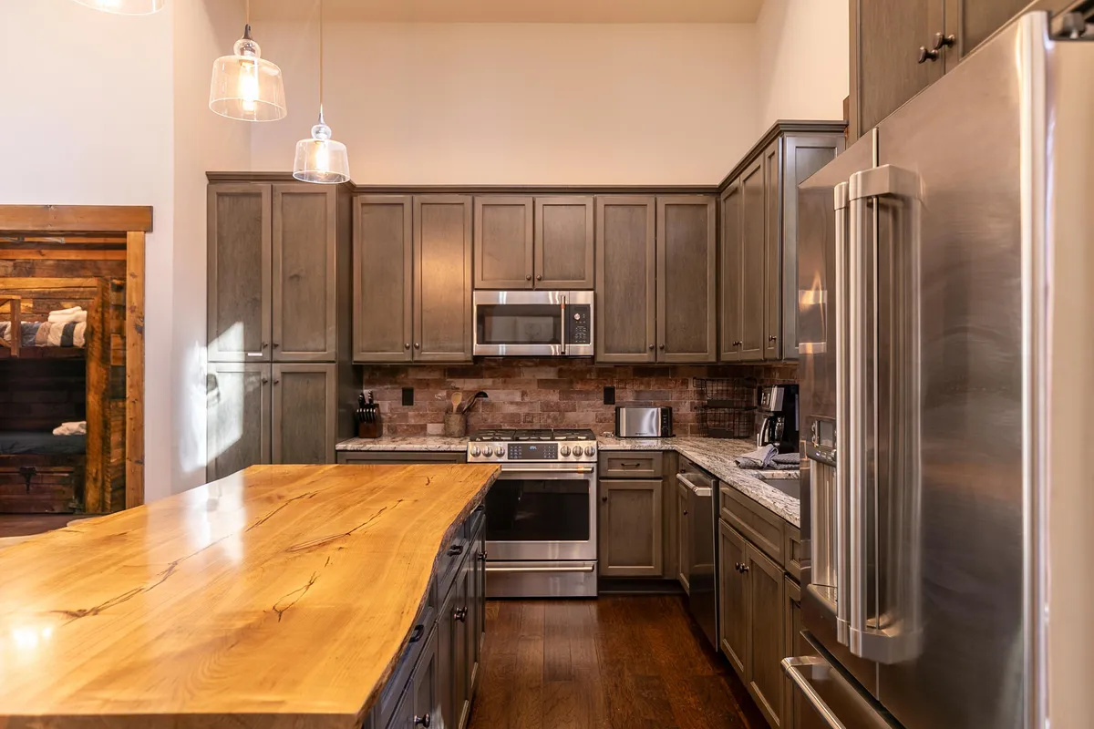 A spacious kitchen is highlighted by a large wooden island surrounded by seating, stainless steel appliances, and granite countertops. The layout exudes warmth and functionality, inviting group meal prep and lively conversation.
